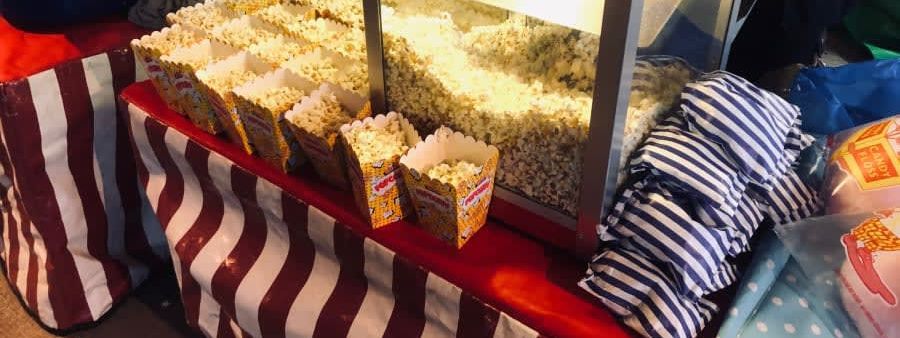 Striped fairground snack cart with a glass-fronted popcorn machine and rows of filled striped cartons