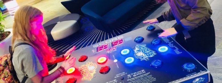 Two players competing head-to-head on the Strike a Light reaction table with red and blue illuminated dome buttons