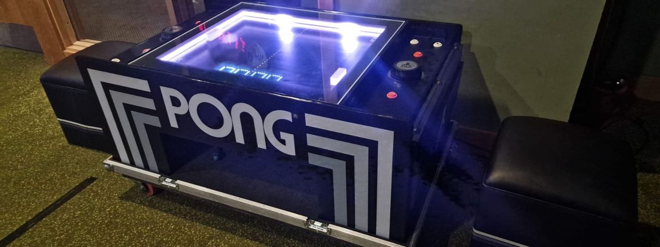 Atari Pong table on flight-case wheels with the playfield lit up