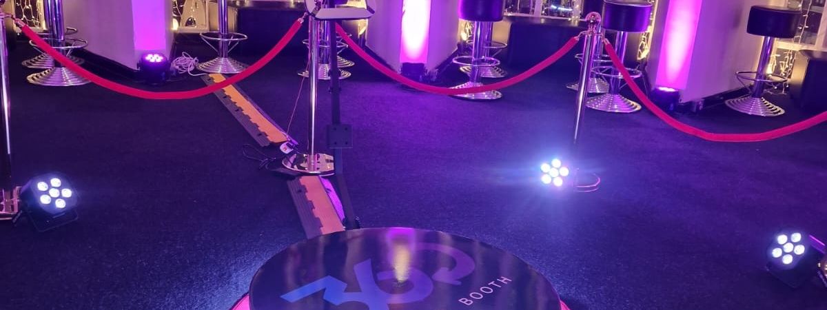 360 photobooth platform with LED-lit ring, roped stanchions and fairy lights set up at an event venue