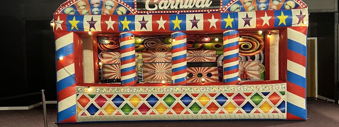 Grand carnival fun fair stalls under spotlit stage lighting at an evening corporate event