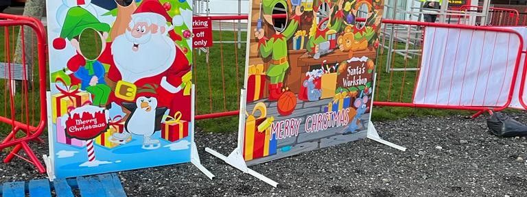 Santa & Child photo cut-out board next to a Santa's Workshop board at an outdoor event