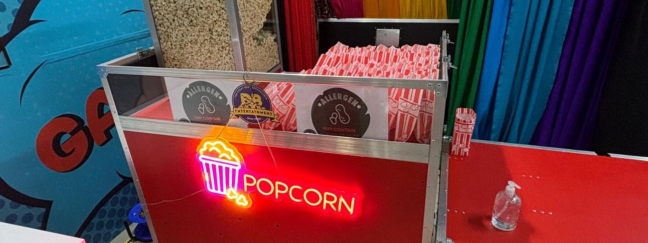 Red flight-case popcorn cart with a lit neon popcorn sign and a glass display case full of popcorn