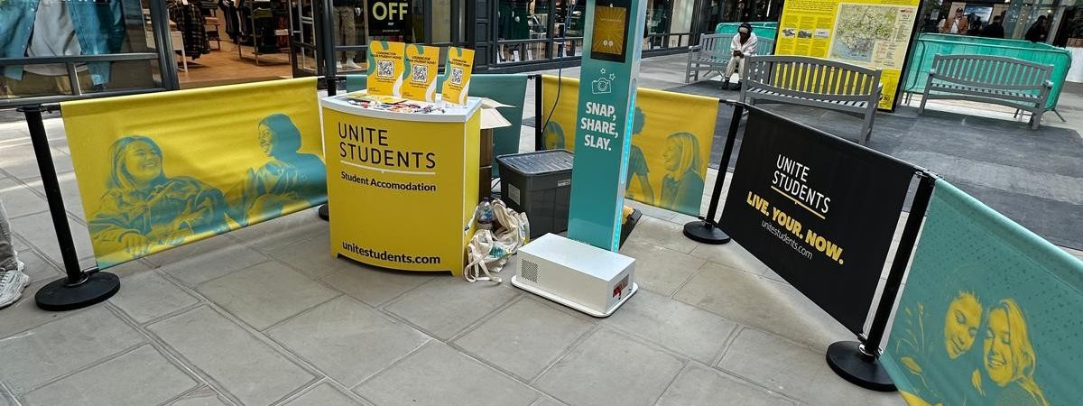 Branded Unite Students photo booth stand inside a busy university shopping mall