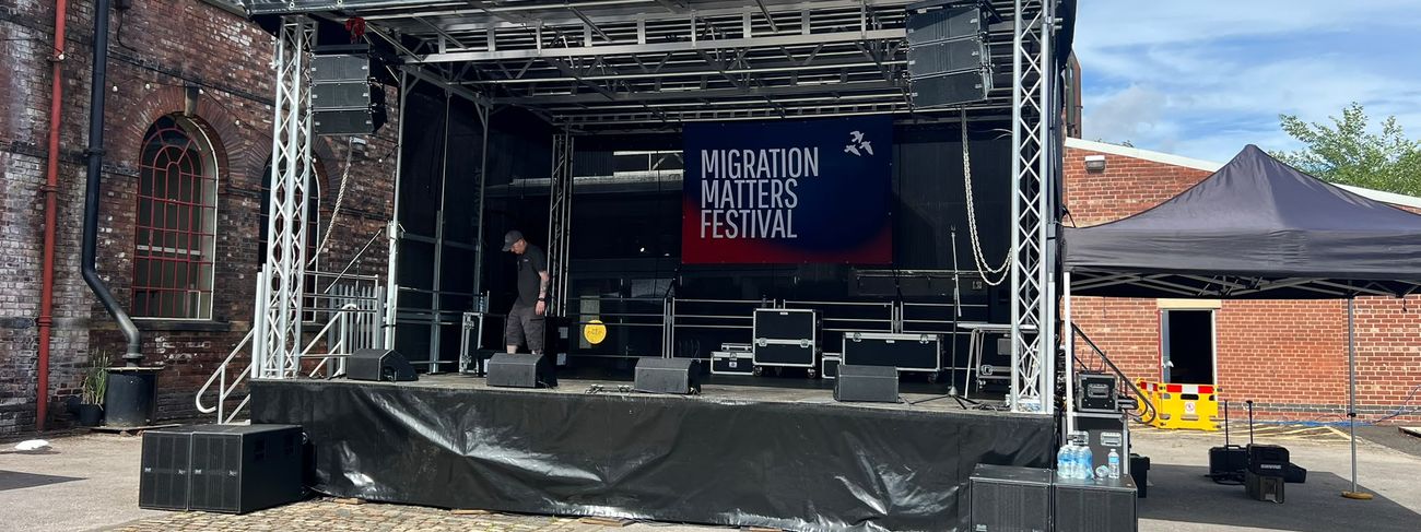 Covered 7x6m mobile trailer stage with line-array PA set up outside Kelham Island Museum for the Migration Matters Festival outdoor stage