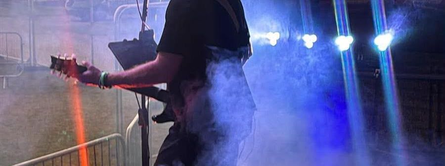 Guitarist silhouetted against a sunset on one of our stages, with stage haze and blue lighting
