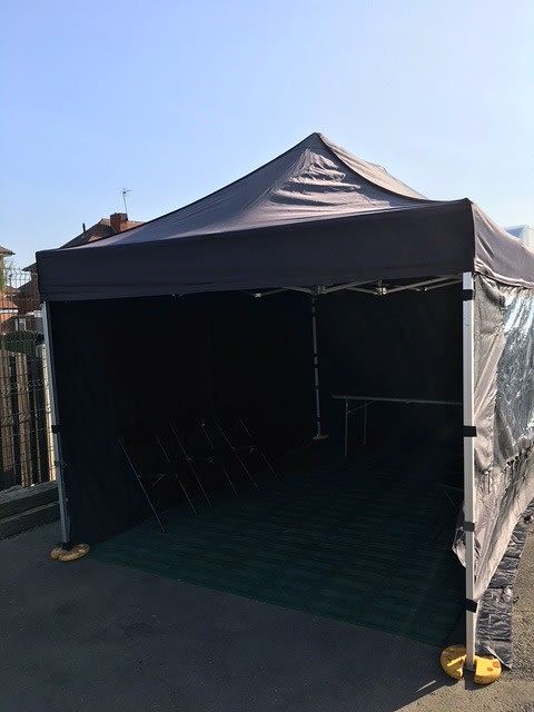Black 3x3m gazebo with side panels set up outdoors with chairs inside