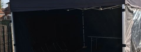 Black 3x3m gazebo with side panels set up outdoors with chairs inside