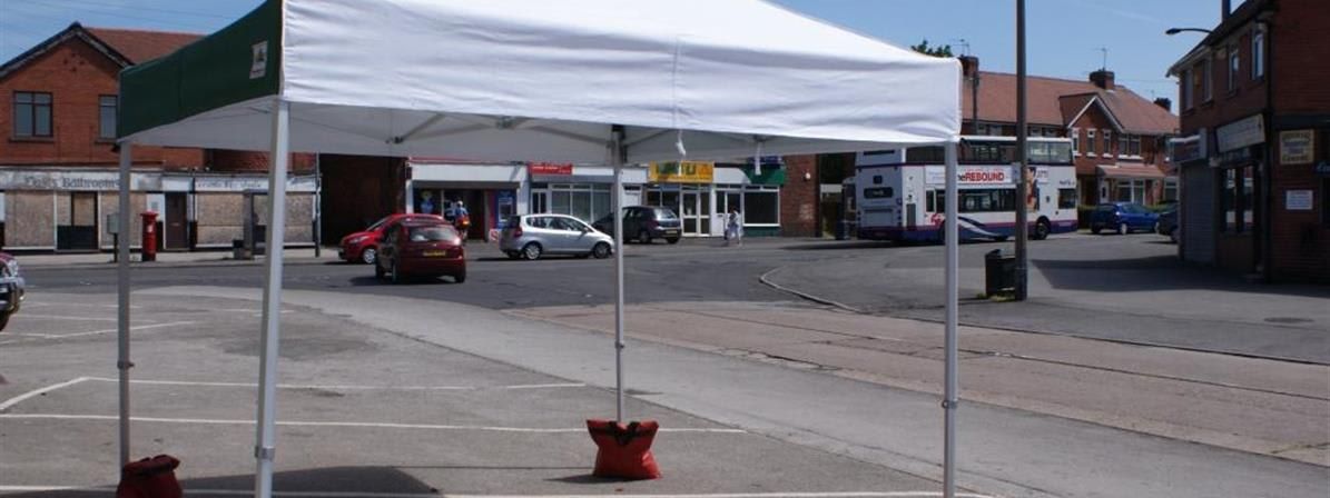 White and green 3x3m pop-up gazebo with weighted feet on a town centre street