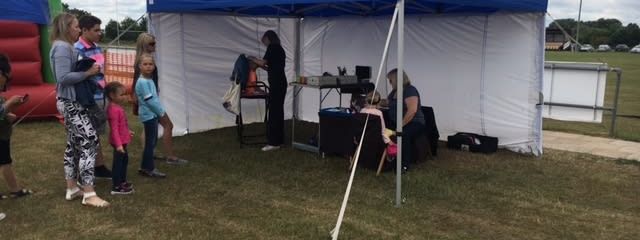 Blue-roofed pop-up gazebo with white side walls set up on grass at a community event
