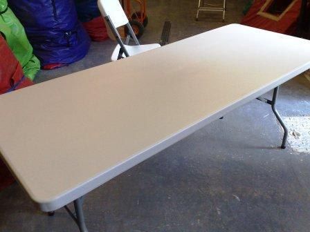 Angled view of a beige 6ft folding table in a storage area