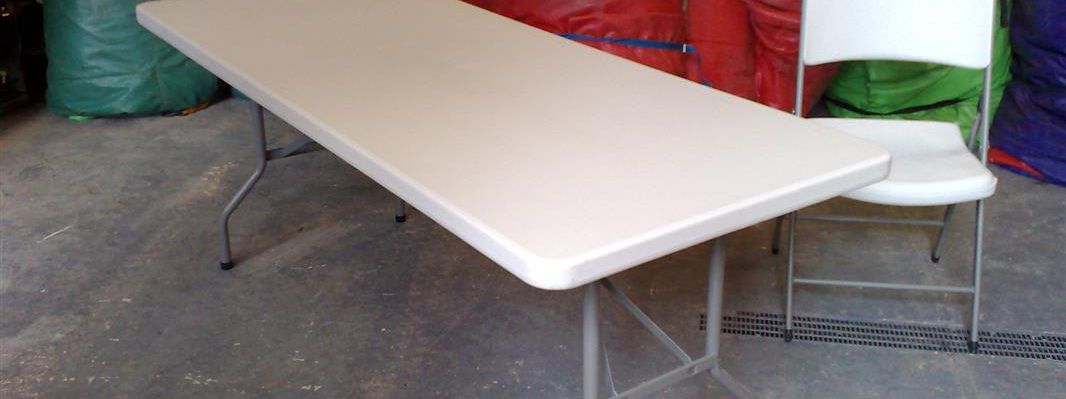 White rectangular 6ft folding table with a chair beside it in a hire warehouse
