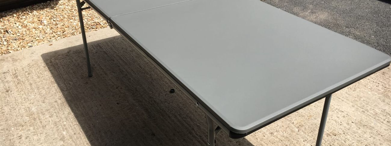 Grey 6ft fold-in-half table on a driveway in front of a storage area