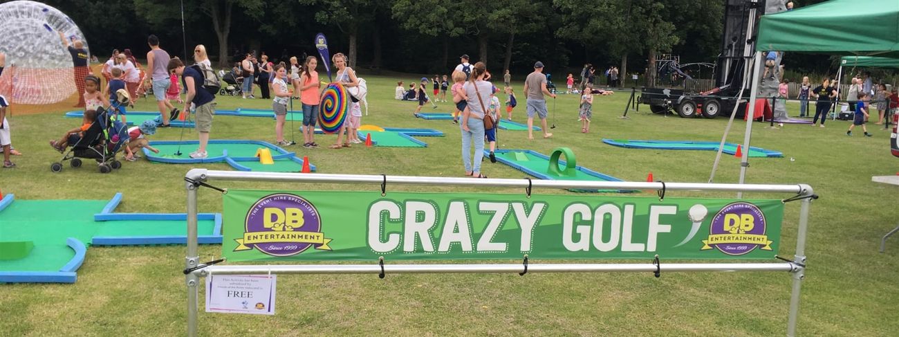 Branded green Crazy Golf banner fronting a busy outdoor course at a park fete