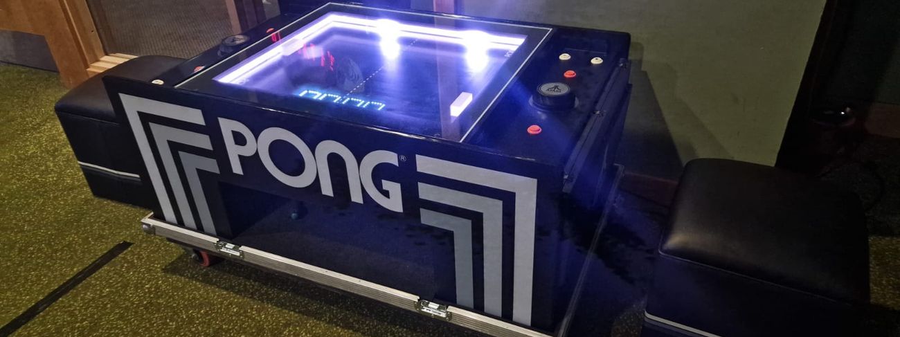 Atari Pong table on its wheeled flight-case base with a seat alongside, the playfield lit blue