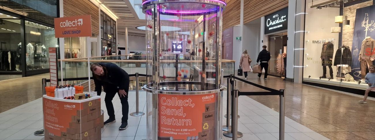 Collect+ and Love2Shop branded Ballnado Grabber with orange header and lower wrap in a shopping centre