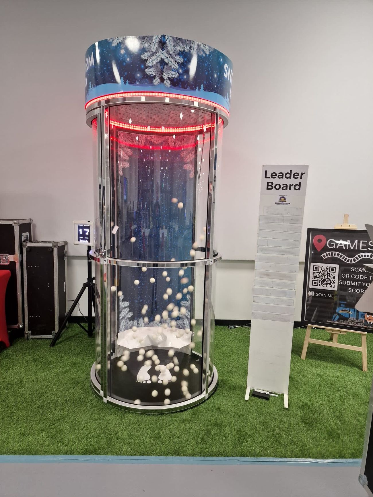 Snow Storm Ballnado with white foam balls swirling inside the cylinder, red LED lighting, and a winter-themed backdrop