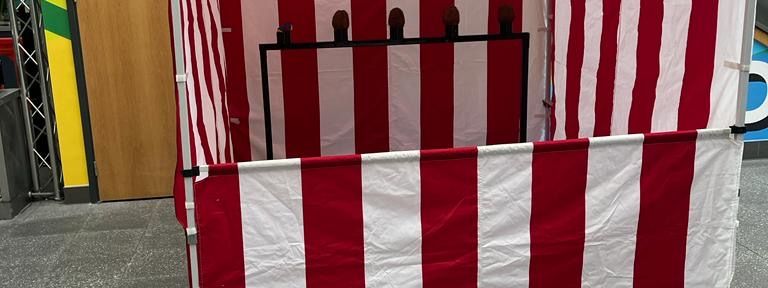 Traditional coconut shy stall with coconuts balanced on red and white posts under a striped canopy