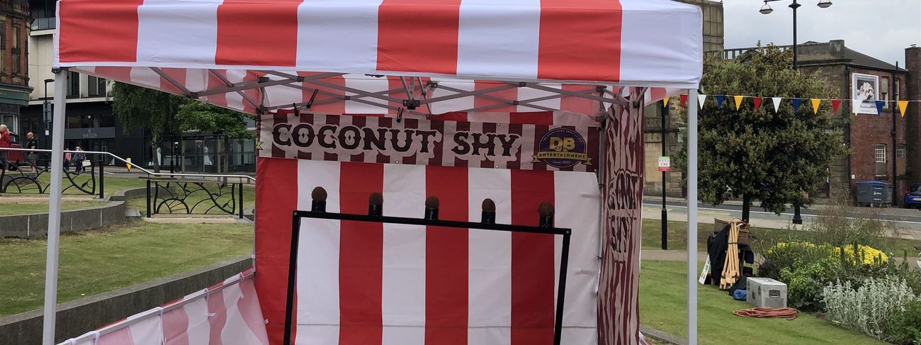 Red and white striped coconut shy stall with five real coconuts on a black target stand
