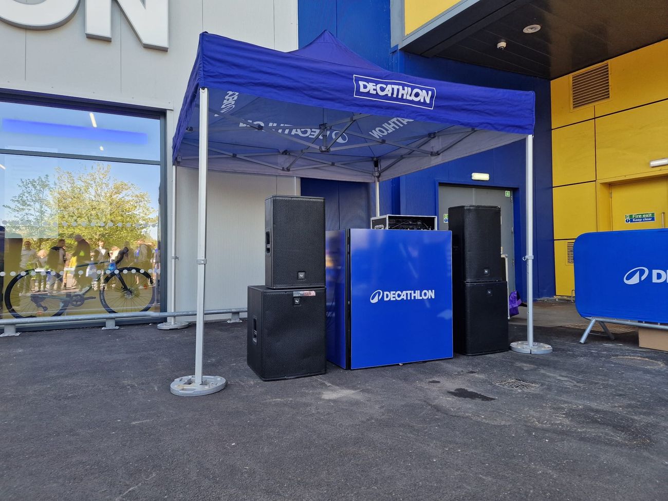 Branded DJ booth with a pair of PA tops on subwoofers either side, set up under a gazebo