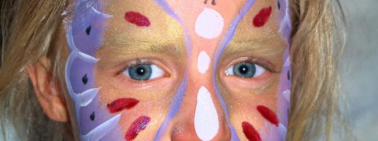 Full-face gold and purple butterfly face paint on a young girl