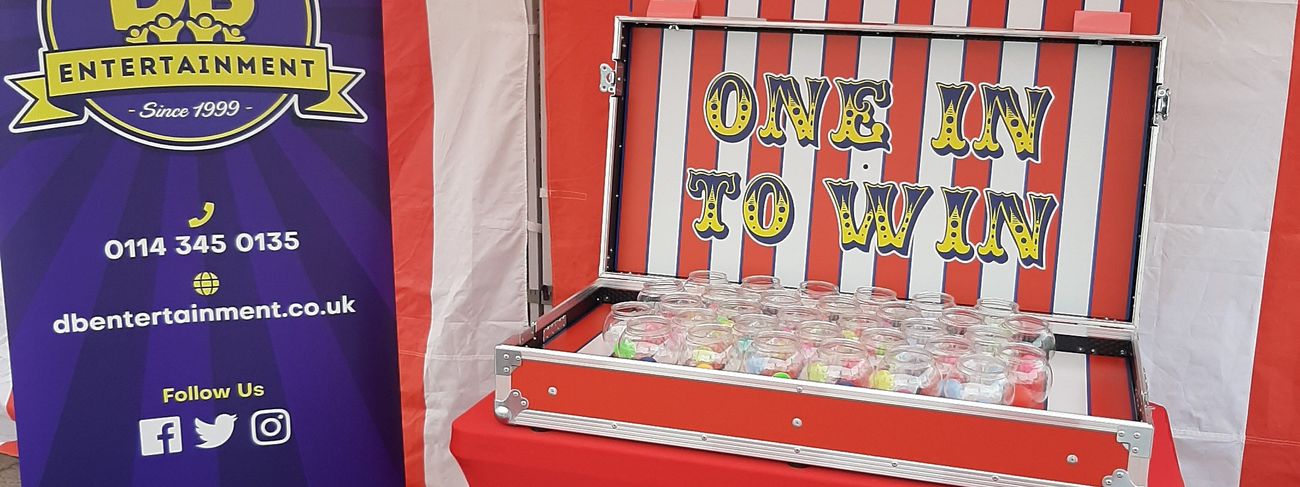 Fish Bowl Challenge side stall under a red and white striped canopy with the One In To Win flight case on the table