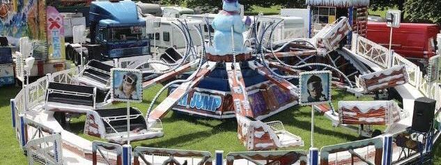 Giant Ski Jump funfair ride with circular cars on arms around a central snowman figure and SKI JUMP lettering on the back board, set up on grass