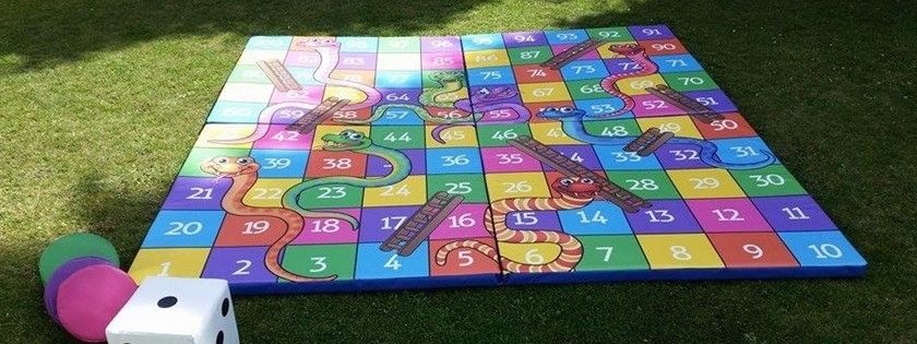 Giant printed Snakes and Ladders floor mat with an oversized foam die at a family event