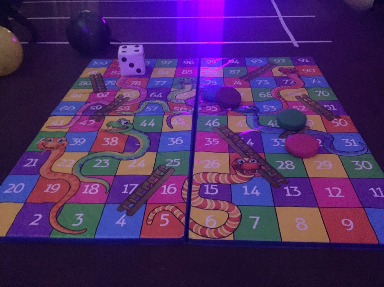 Children rolling a large foam die on a giant Snakes and Ladders mat on grass