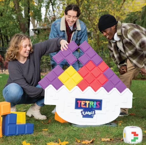A player placing a purple Tetrimino block on the white Tetris Tumble base while two others watch