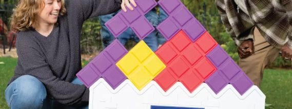 Players stacking oversized Tetrimino blocks on the white moulded Tetris Tumble base on a lawn