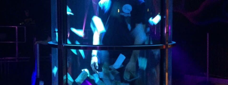 A player grabbing vouchers inside the lit Grab a Grand tank under blue and purple stage lighting