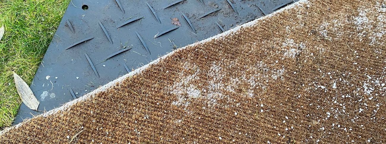 Black HDPE mat alongside coir matting on grass