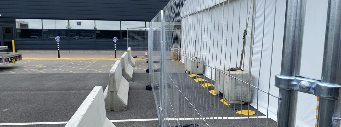 Run of galvanised round-top temporary fence panels alongside an event marquee