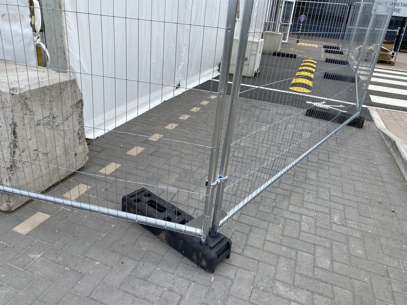 Two galvanised mesh fence panels joined by a coupler clip on weighted block feet