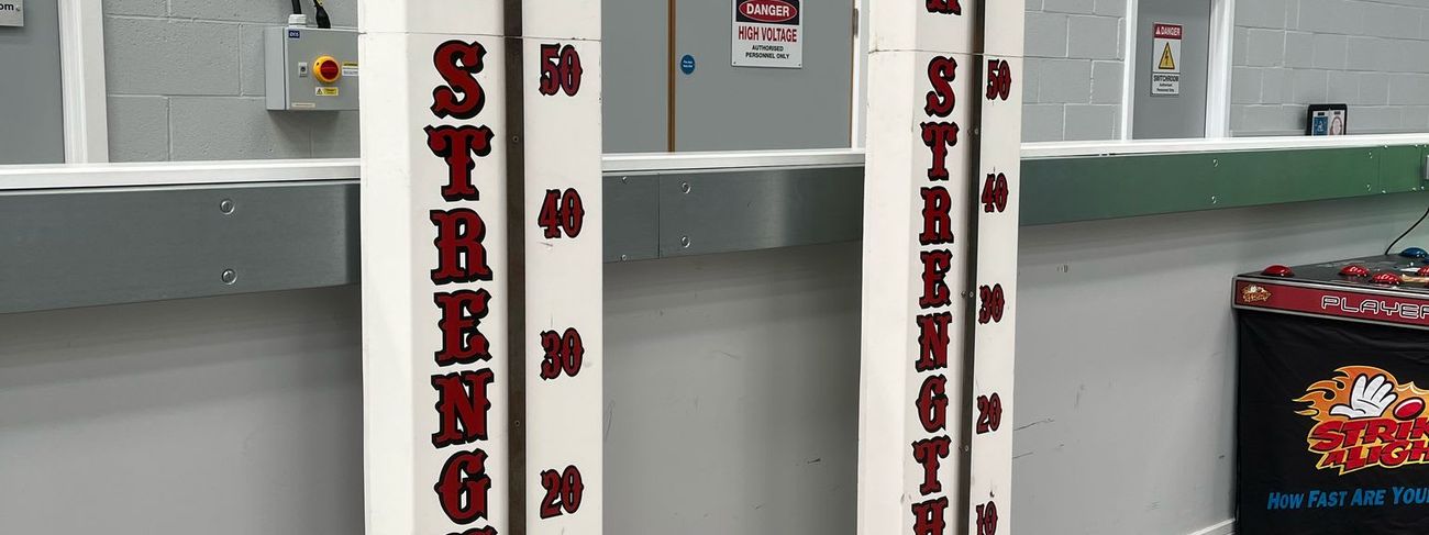 Two white Test Your Strength high striker towers with red bases and a giant mallet in the DB Entertainment warehouse