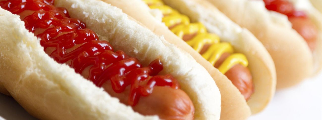 Row of jumbo frankfurters on giant buns topped with ketchup and mustard zigzags