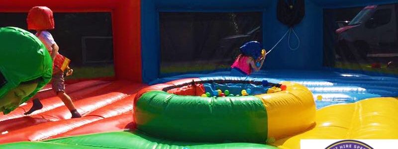 Players on wheeled boards lunging into a central ball pit on an inflatable Hungry Hippos arena