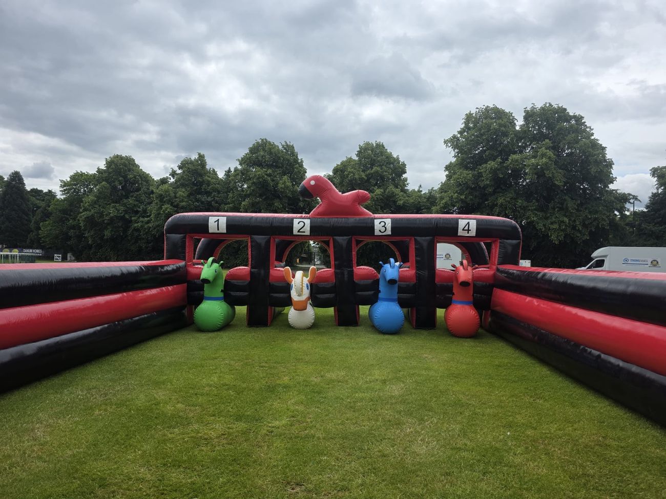 Four inflatable hopper horses - green, white, blue and red - lined up in the numbered one-to-four starting pens beneath a red inflatable horse figure