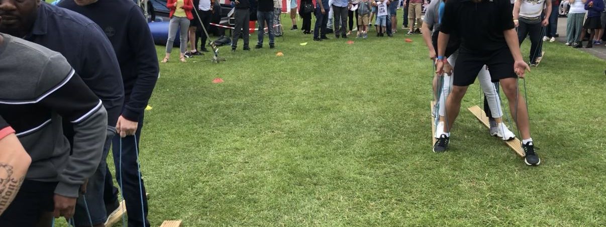 Teams racing on wooden giant skis using individual blue hand ropes