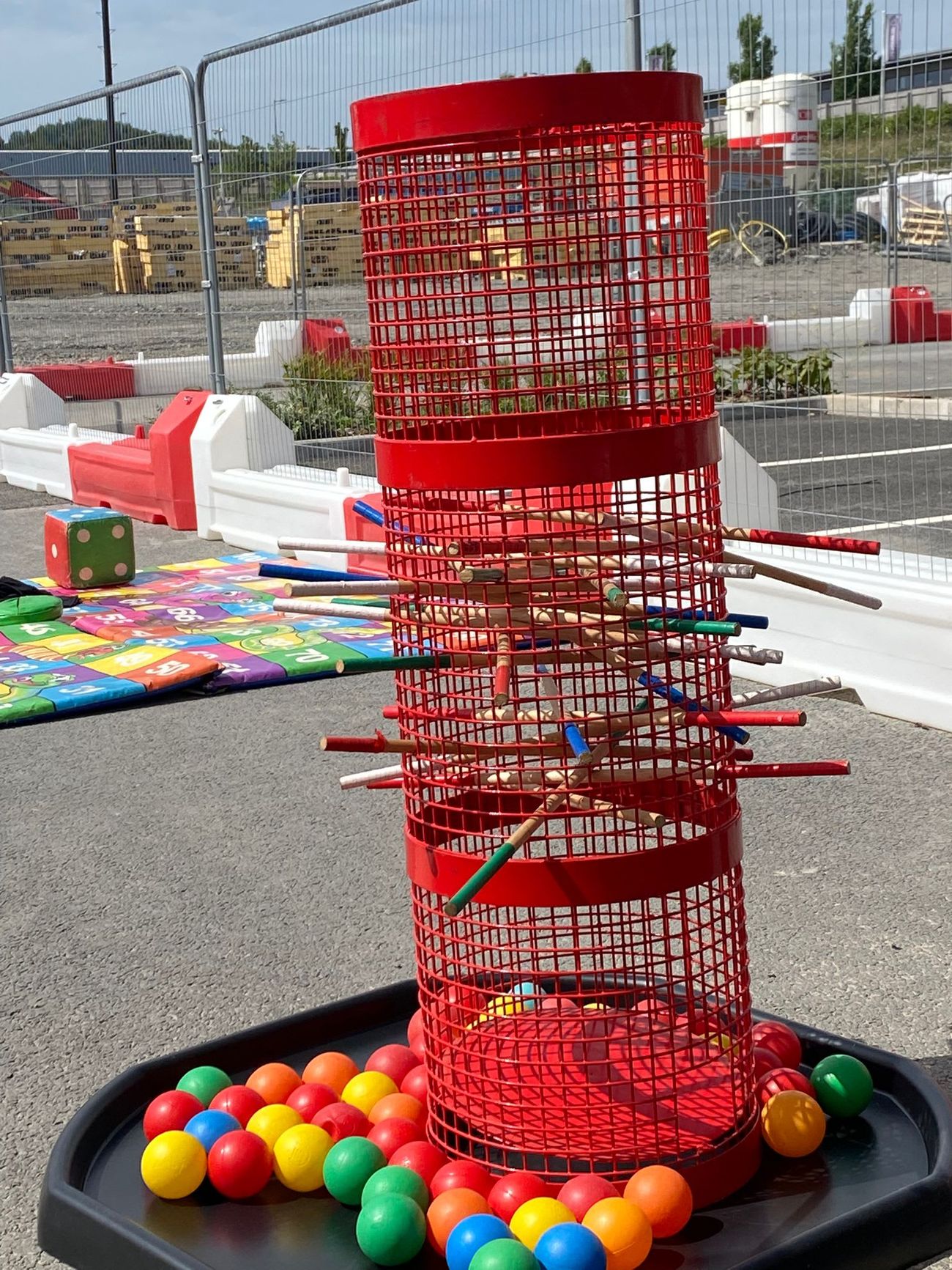 Mega Kerplunk red mesh tower outdoors with coloured balls and rods, plus a giant dice on a play mat