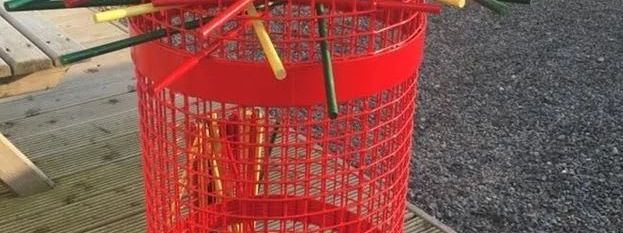 Red cylindrical mesh tower filled with colourful balls and crisscrossing wooden sticks