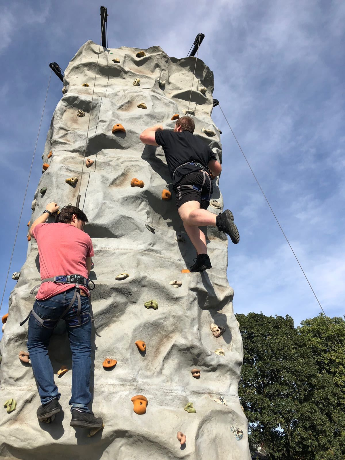 Two climbers on the 26ft mobile climbing wall with the auto belay frames above them