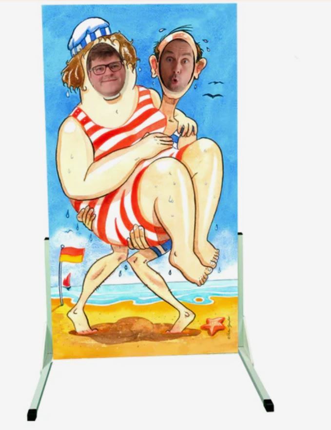 Vintage seaside face-in-the-hole board with a skinny man in blue-and-white striped trunks carrying a much larger woman in a red-and-white striped bathing suit and sailor-style hat, one face hole in each head, against a beach scene with waves, a sailboat and a lifeguard flag