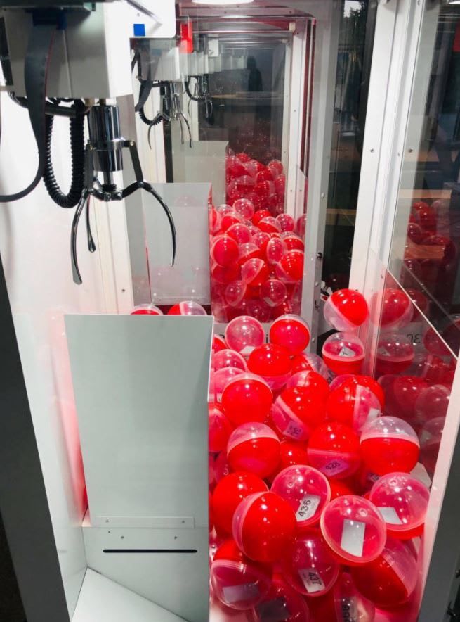 Close-up of claw above red capsule prizes