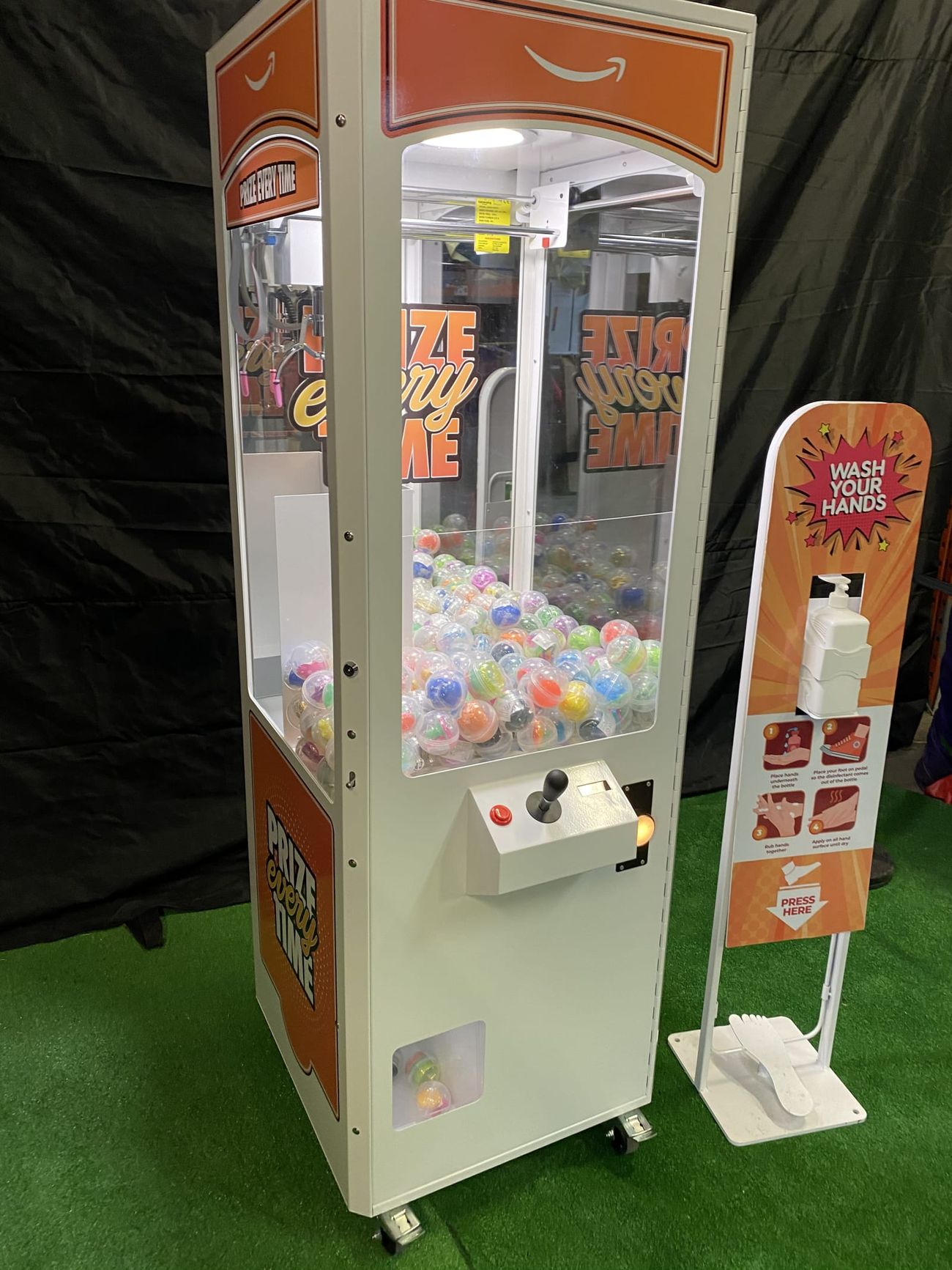 White prize crane arcade grabber with Amazon branding, red capsule prizes and internal LED lighting