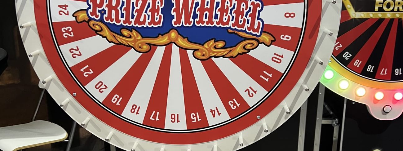 Red and white circus-style Prize Wheel with a lit bulb rim beside an LED Wheel of Fortune at an event