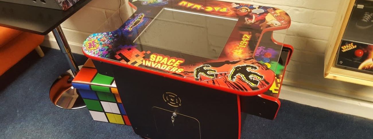 Black retro cocktail arcade cabinet with red trim and classic game artwork under the glass top, in our showroom