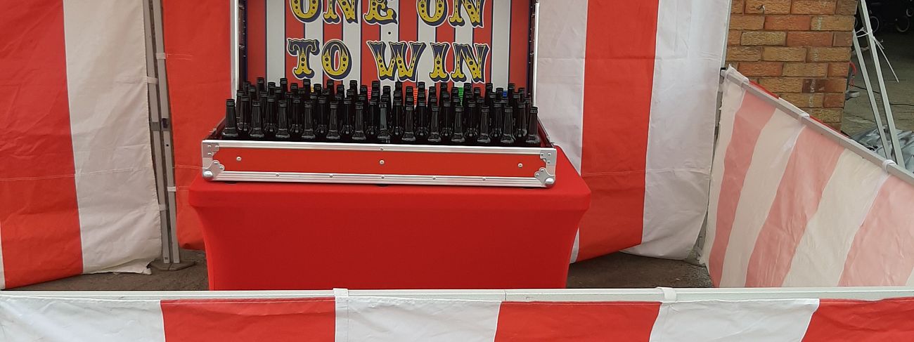Ring Toss bottle board beneath the One On To Win lid inside its red and white striped marquee