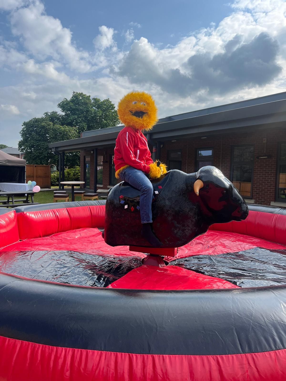 Event mascot riding a black mechanical bull in a red-and-black inflatable bed